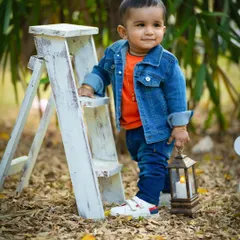 A stylish little dude in his denim jacket, posing by a ladder prop in a beautiful park. Outdoor sessions are great for capturing active toddlers.