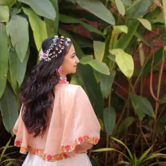 A whimsical and romantic hairstyle for a Haldi carnival. This look features soft waves adorned with a custom floral and beaded headpiece, creating a beautiful bohemian vibe from the back.
