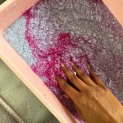 Experimenting with adding natural dyes to my paper pulp. Here, I'm swirling in a beautiful magenta pigment to create colored, recycled paper sheets.