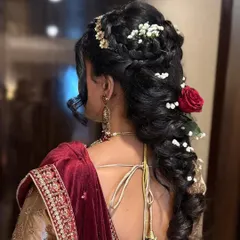 A detailed look at an intricate bridal hairstyle from the back. This style combines braids, curls, and floral accessories, creating a stunning and secure updo perfect for supporting a dupatta and lasting through the entire celebration.