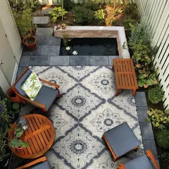 Even a compact backyard can become a personal oasis. This design utilizes vertical space with climbing plants and a raised pond with water lilies. The seating area, defined by an outdoor rug, creates a cozy and inviting corner for relaxation.