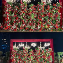 A truly dramatic reception stage featuring a dense wall of red florals and lush greenery, crowned with elegant crystal chandeliers. This design creates an atmosphere of pure opulence and romance for a grand celebration.