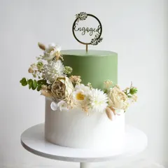 A modern and chic two-tier engagement cake in a trendy sage green and white. The design is elevated with a beautiful arrangement of fresh, natural-toned flowers for a sophisticated look.