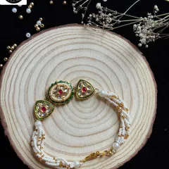 An elegant kundan rakhi with red and green stones set in a delicate pearl and bead strand. This timeless design adds a touch of royalty to the sacred thread.
