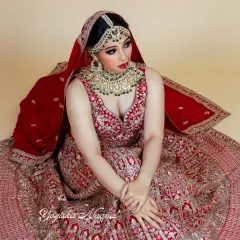 A full view of a modern bride in a traditional red lehenga. The makeup is balanced to complement the heavy embroidery and jewelry, ensuring the bride's natural beauty remains the centerpiece.