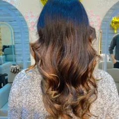 A soft balayage with natural brown and caramel tones, styled with gentle waves for a sophisticated look.