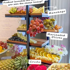 A closer look at the tiered cheese tower from the Bioderma event, featuring Manchego and Gouda cheeses, marinated olives, and fresh fruits.
