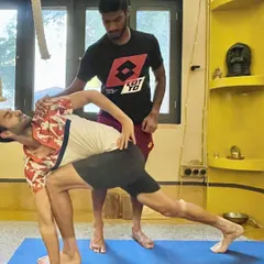 Here, a professional tennis player receives an adjustment in Parivrtta Parsvakonasana (Revolved Side Angle Pose). This hands-on guidance helps deepen the twist and open the chest, which is crucial for rotational power and flexibility in sports like tennis.