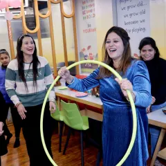 The pure joy of game time. This photo captures the laughter and excitement as a guest plays a hula hoop game during a party, surrounded by her cheering friends.