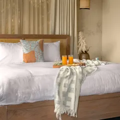 A close-up of the bed, showing the simple, high-quality linens and the natural textures of the woven cane headboard. Every detail is chosen to complement the serene, wabi-sabi aesthetic of the mountain retreat.