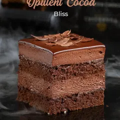 Meet the Opulent Cocoa Bliss, a multi-layered chocolate pastry. It combines dense chocolate sponge with silky chocolate mousse and is topped with delicate chocolate shavings for a rich and satisfying experience.