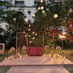 A cozy and romantic outdoor seating area. We designed this photo booth with a pink sofa, a golden lattice backdrop, and an array of candles and hanging lights for a magical evening ambiance.