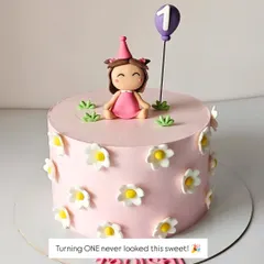 A simple and sweet first birthday cake. The design features a fondant girl topper, a single balloon, and delicate daisy flowers, perfect for an intimate celebration.
