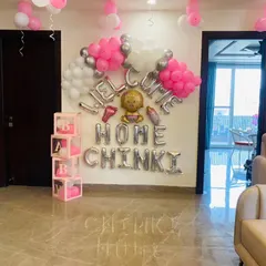 A personalized "Welcome Home Chinki" decoration to make the moment unforgettable. This setup uses silver foil letter balloons, pink 'BABY' blocks, and clusters of pink and silver balloons to create a loving atmosphere.