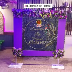 A unique photo backdrop featuring a green grass wall with a purple frame. The top is adorned with purple flowers, and a custom gold-acrylic sign with my brand name is placed in the center.