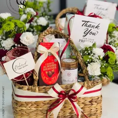 A beautiful thank you hamper presented in a woven basket. It combines fresh flowers with gourmet treats like choco-almond dragees, making it a warm and heartfelt way to show appreciation.