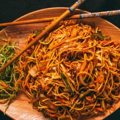 A plate of my delicious Hakka noodles, stir-fried with fresh vegetables and served on a wooden platter. A simple, classic, and satisfying dish.