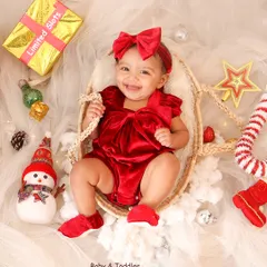 The perfect Christmas card photo. This baby's joyful smile, festive red outfit, and the surrounding holiday props create a picture of pure holiday cheer.