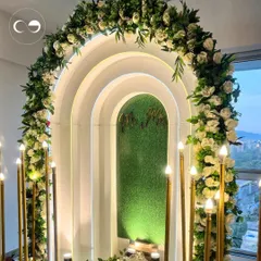 The warm glow of candle-style floor lamps adds a magical ambiance to this indoor engagement setup. The combination of florals, greenery, and lighting creates a sophisticated and inviting atmosphere.