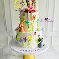 Whiskers, flowers, and birthday magic. This adorable two-tier cake is bursting with charm, featuring playful cats, blooming flowers, butterflies, and a sweet little doll topper.