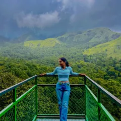 A trekker standing on the glass bridge at 900 Kandi in Wayanad, with a stunning view of the green valley below.