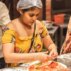 A participant concentrates on adding fresh basil to her pizza base. Our workshops guide you through every step of creating a classic Neapolitan pizza.