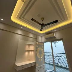 This bedroom corner was designed to be multi-functional. It includes a custom-built study desk with illuminated shelves, alongside a beautifully crafted pooja unit with a CNC-cut 'Swastik' panel. The multi-layered false ceiling with cove lighting adds a modern, ambient touch.