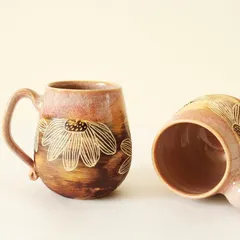 A pair of 'Pink Sienna' mugs, each with its own unique hand-carved floral details. Because they are handmade, no two are ever exactly alike, which is part of their charm.