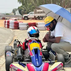 A coach kneels down to talk strategy with a young driver, providing personalized instruction under the shade of an umbrella.