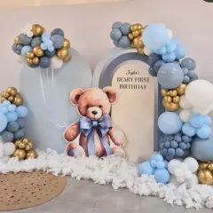 A "Beary First Birthday" theme with a large teddy bear cutout, arched backdrops, and a soft blue, grey, and gold balloon arrangement.