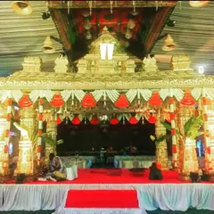 A 'Trupati' style mantap, this stage is designed for large wedding or religious ceremonies, featuring ornate pillars and traditional red and white floral hangings.