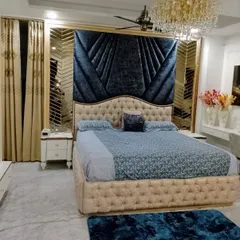 A master bedroom designed for pure luxury and comfort. The deep blue velvet headboard creates a dramatic focal point, complemented by a stunning crystal chandelier and custom mirrored panels, proving that a bedroom can be both a restful sanctuary and a statement of style.