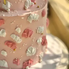 A close-up detail of the pink first birthday cake, showing the texture of the palette-knife buttercream petals and the scattered edible pearls.
