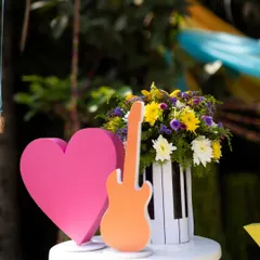 A vibrant centerpiece from a music-themed party, featuring a colorful floral arrangement in a piano-key vase, flanked by a bright pink heart and an orange guitar cutout.