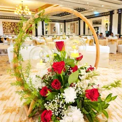 This unique table centerpiece features a circular wooden frame with red and white flowers and hanging glass orbs with tea lights for a rustic yet modern look.