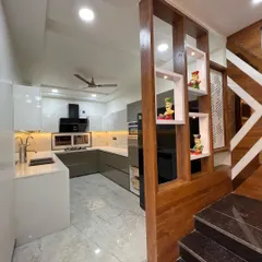 A wooden partition with built-in display shelves elegantly separates the kitchen from the staircase area. This design adds warmth and a personal touch while maintaining the open feel of the space.