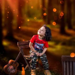 A young boy sits in a forest clearing, looking up at magical glowing lights. This outdoor photo combines natural beauty with a touch of fantasy to create a captivating image.