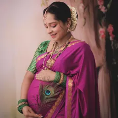 A beautiful and serene traditional portrait. The mom-to-be holds a peacock feather, a symbol of grace and beauty, complementing her elegant pink and green silk saree.