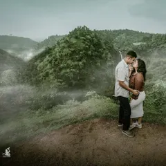 A romantic moment shared between a couple on a misty hilltop, with a stunning waterfall and lush green valley in the background. A perfect example of a destination pre-wedding shoot.