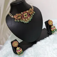 A sophisticated Jadau choker with peacock motifs, ruby and emerald stones, and a pearl border. The matching jhumkas complete this elegant set, which is perfect for a bride or her sister's reception.
