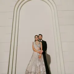 An elegant and classic Sangeet portrait. The couple stands against a minimalist backdrop, letting their stunning outfits and confident connection take center stage.