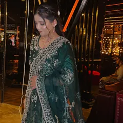 This full-length shot shows the complete party look. The soft makeup and elegant hairstyle perfectly complement the richly embroidered green outfit, creating a sophisticated and put-together appearance.