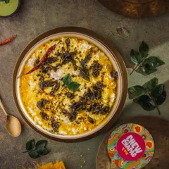 A top-down view of tempered curd rice, styled for Chew Chapad. The dark, moody lighting makes the vibrant yellow of the tempering and the fresh curry leaves pop, emphasizing the dish's comforting yet flavorful nature.