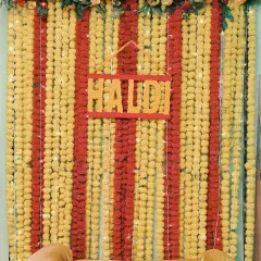 A classic Haldi backdrop for a home function, made entirely of yellow and red marigold flower strings with a custom "Haldi" sign.