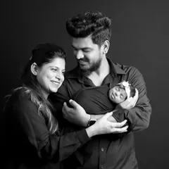 A happy family portrait with both parents and their newborn baby against a classic black backdrop. We guide families into poses that feel natural and showcase their joy and connection.