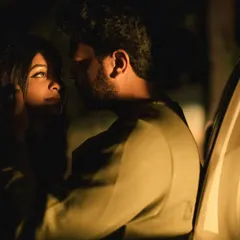 A beautifully lit night portrait. The soft light from the car's open door illuminates the couple's faces as they share an intimate gaze, creating a moody and romantic atmosphere.