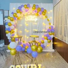 A beautiful and simple birthday setup with a circular frame decorated with pastel purple, gold, and white balloons. The white curtain backdrop with fairy lights creates a soft, dreamy effect, perfect for photos.