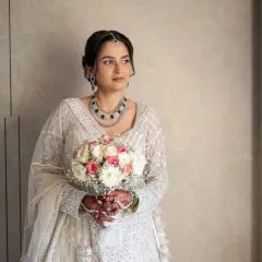 A stunning bridal portrait. The bride holds her bouquet, looking away with a serene expression. This shot highlights her elegant jewelry and the beautiful craftsmanship of her wedding lehenga.