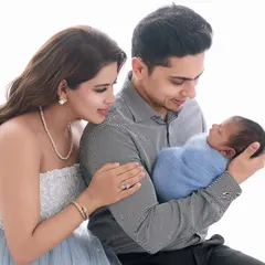 A glowing mother and father admire their newborn, who is wrapped in a soft blue swaddle, creating a bright and joyful family photograph.