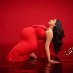 This powerful image captures a moment of pure joy. The mom-to-be, in a striking red gown, leans back into a digitally created water effect, resulting in a unique and artistic maternity photo.